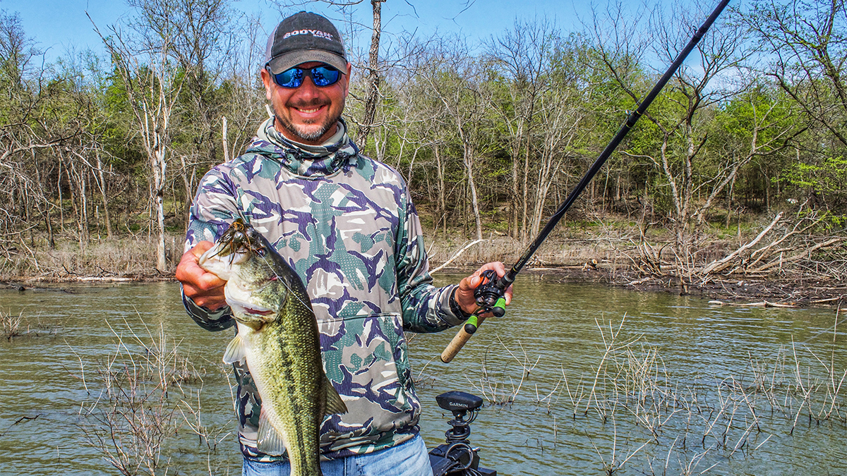 fisherman holding bass in front of flooded cover